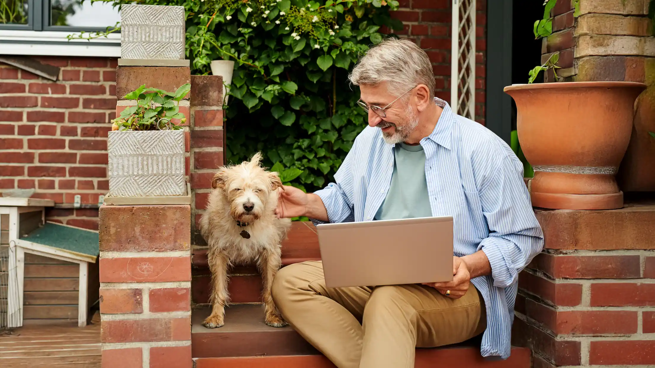 Ein Mann mit Hund sitz Draußen vor einem Laptop